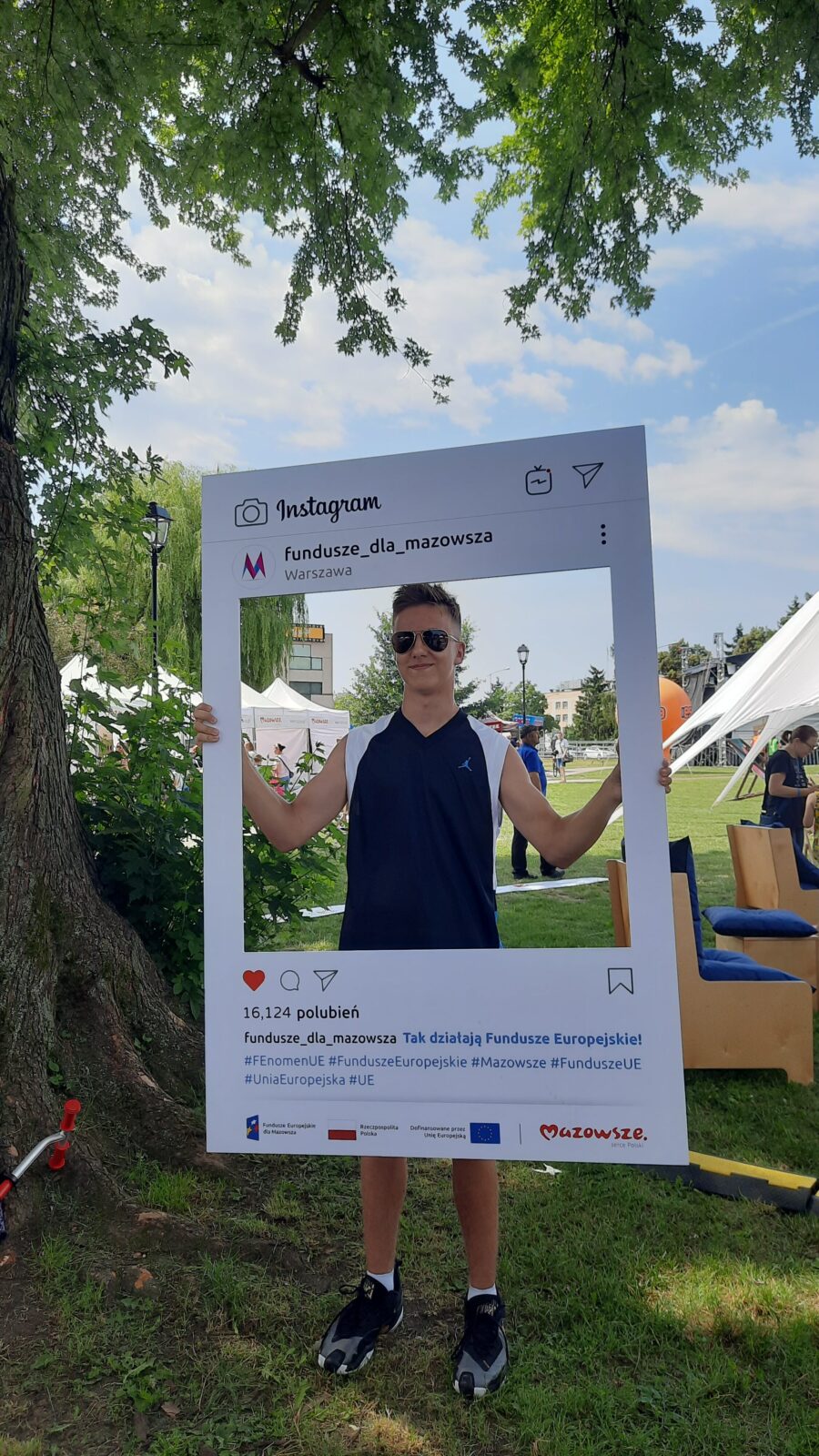 Uczestnik pikniku pozujący z planszą przedstawiającą post na Instagramie profilu Fundusze dla Mazowsza.